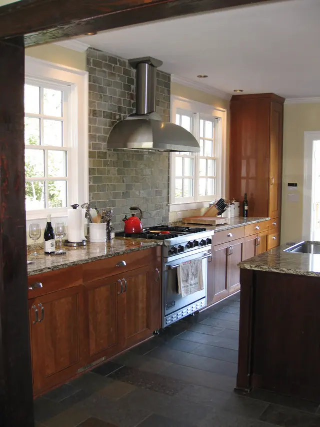 Cherry cabinetry with stone countertops and a professional range under a tile backsplash