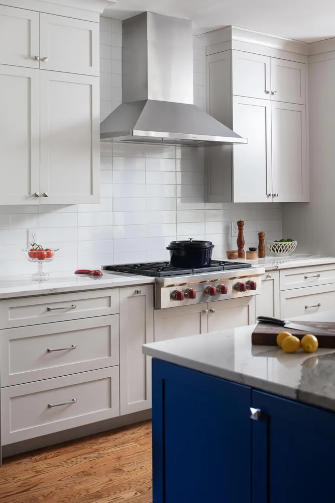 Navy kitchen island with a professional range, marble backsplash, and white shaker cabinetry